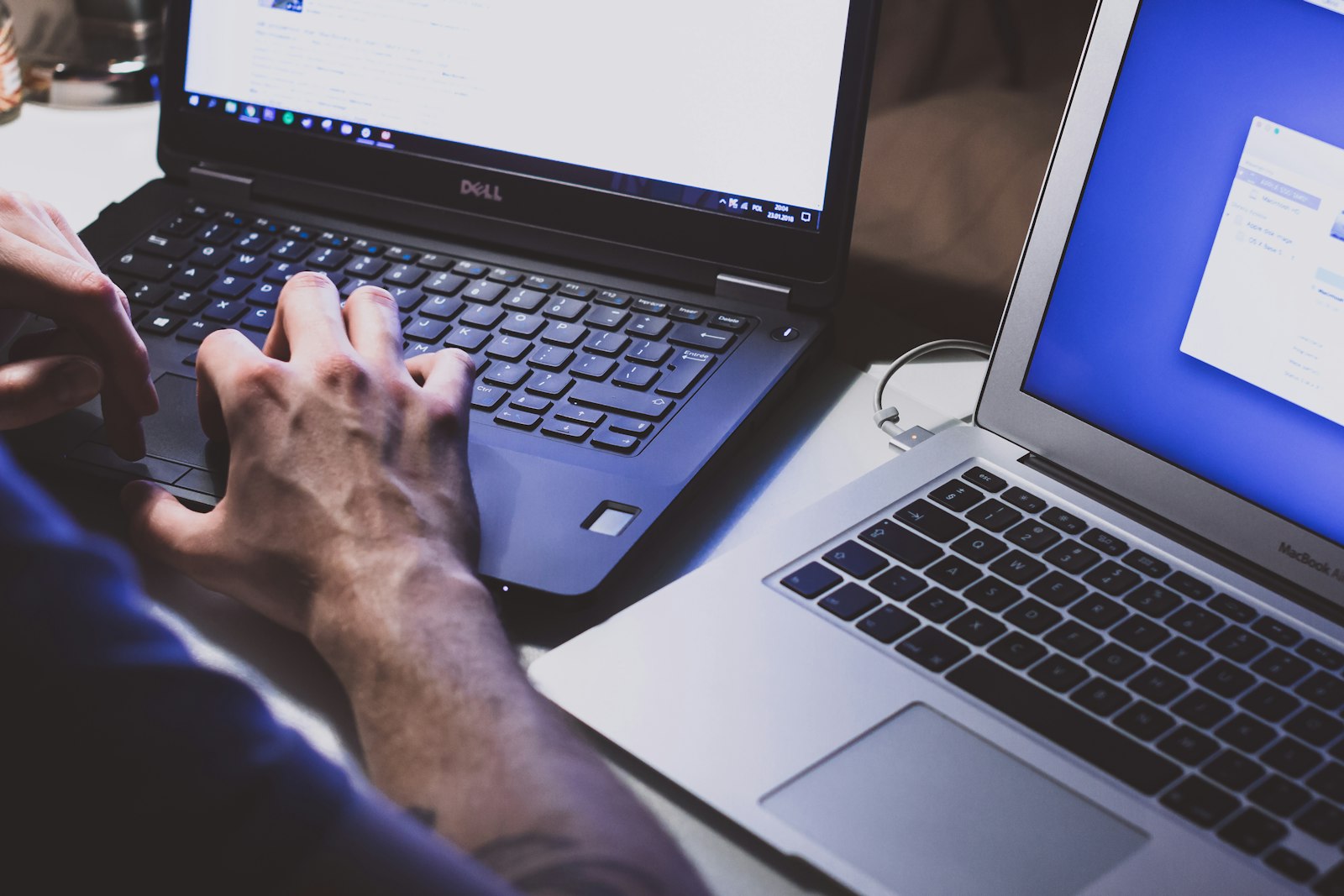 Hands working across two laptops in a dim workspace