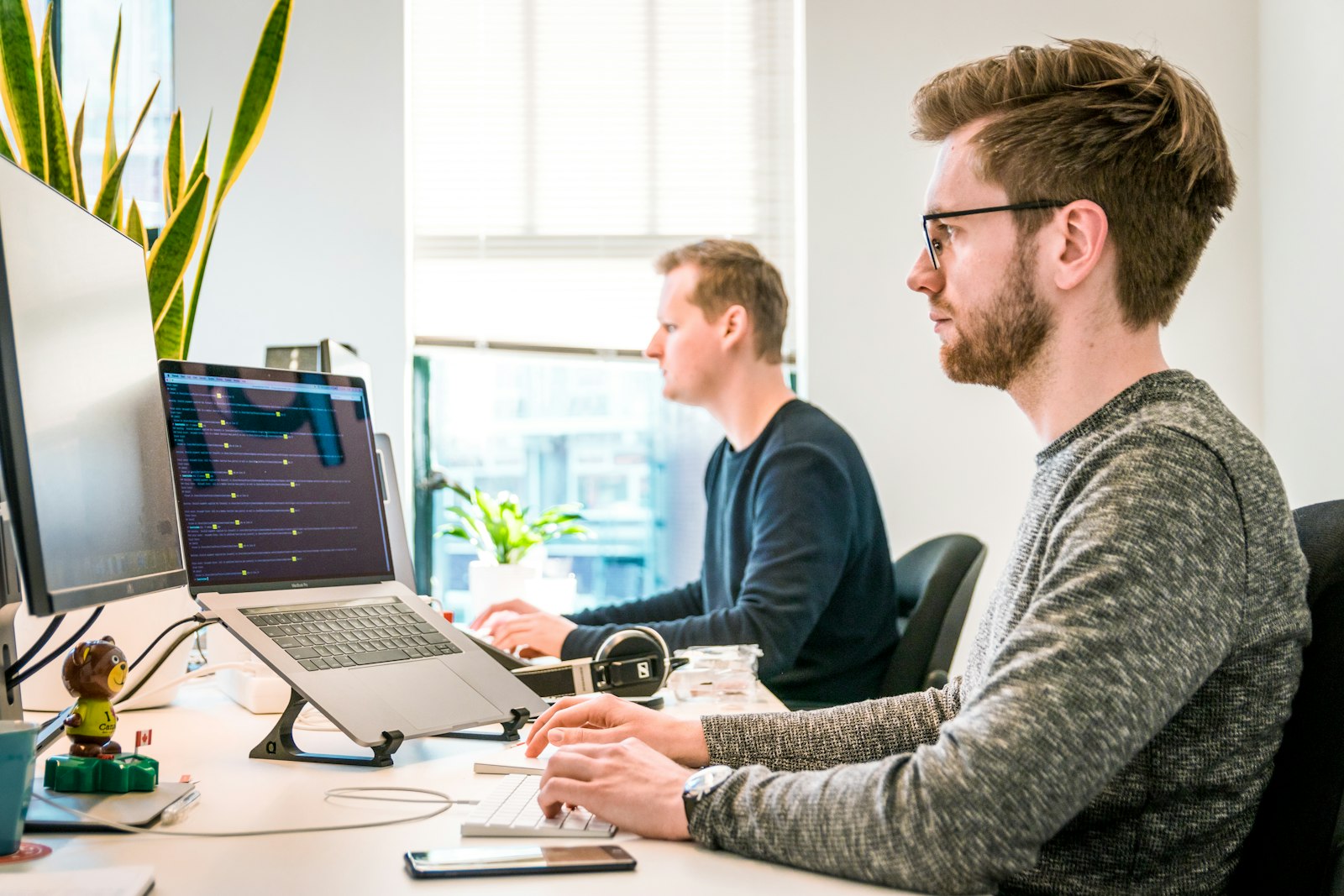 Two software engineers working at a bright office desk with code on a laptop