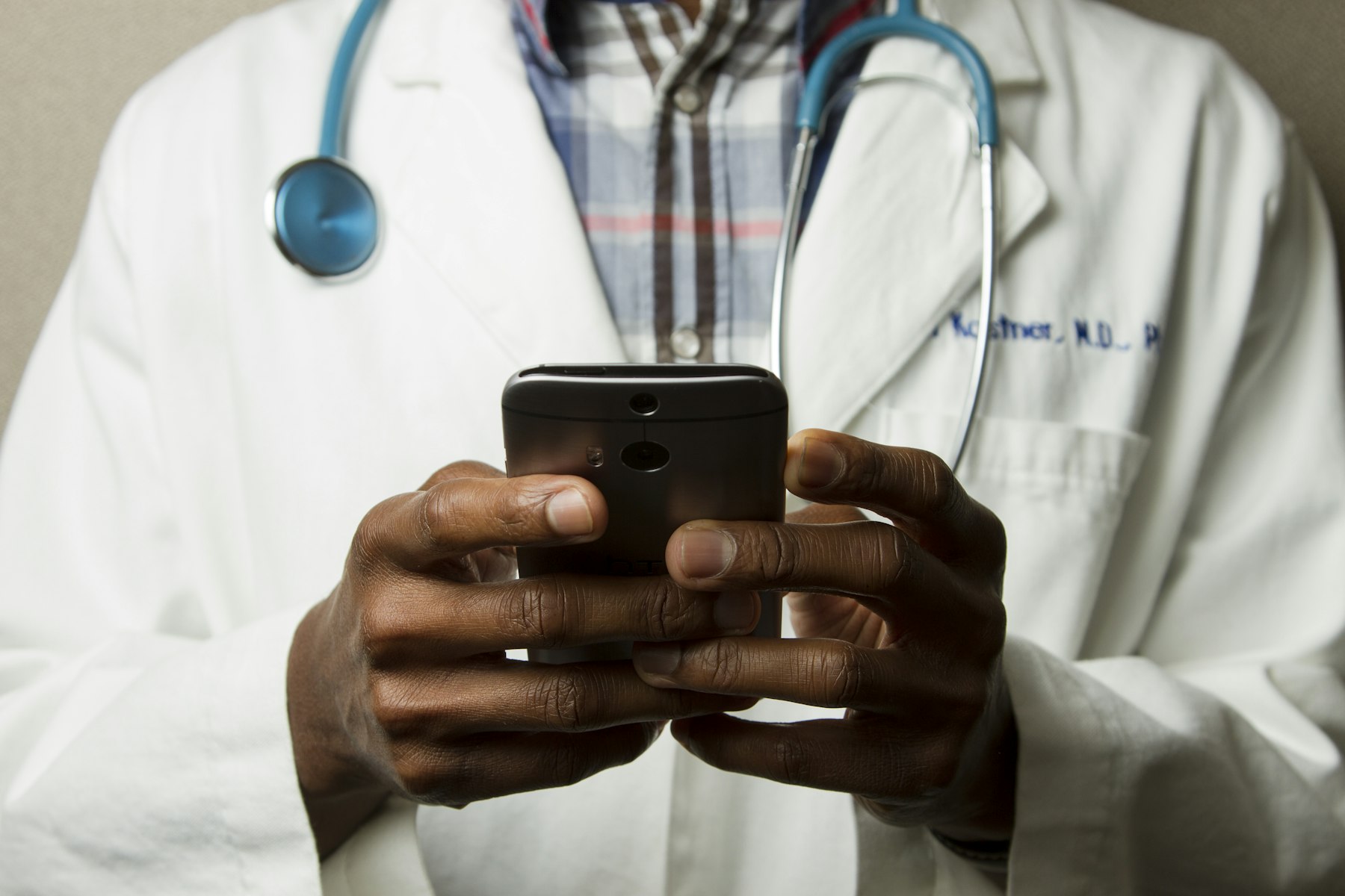 Clinician in a lab coat using a smartphone, stethoscope around their neck